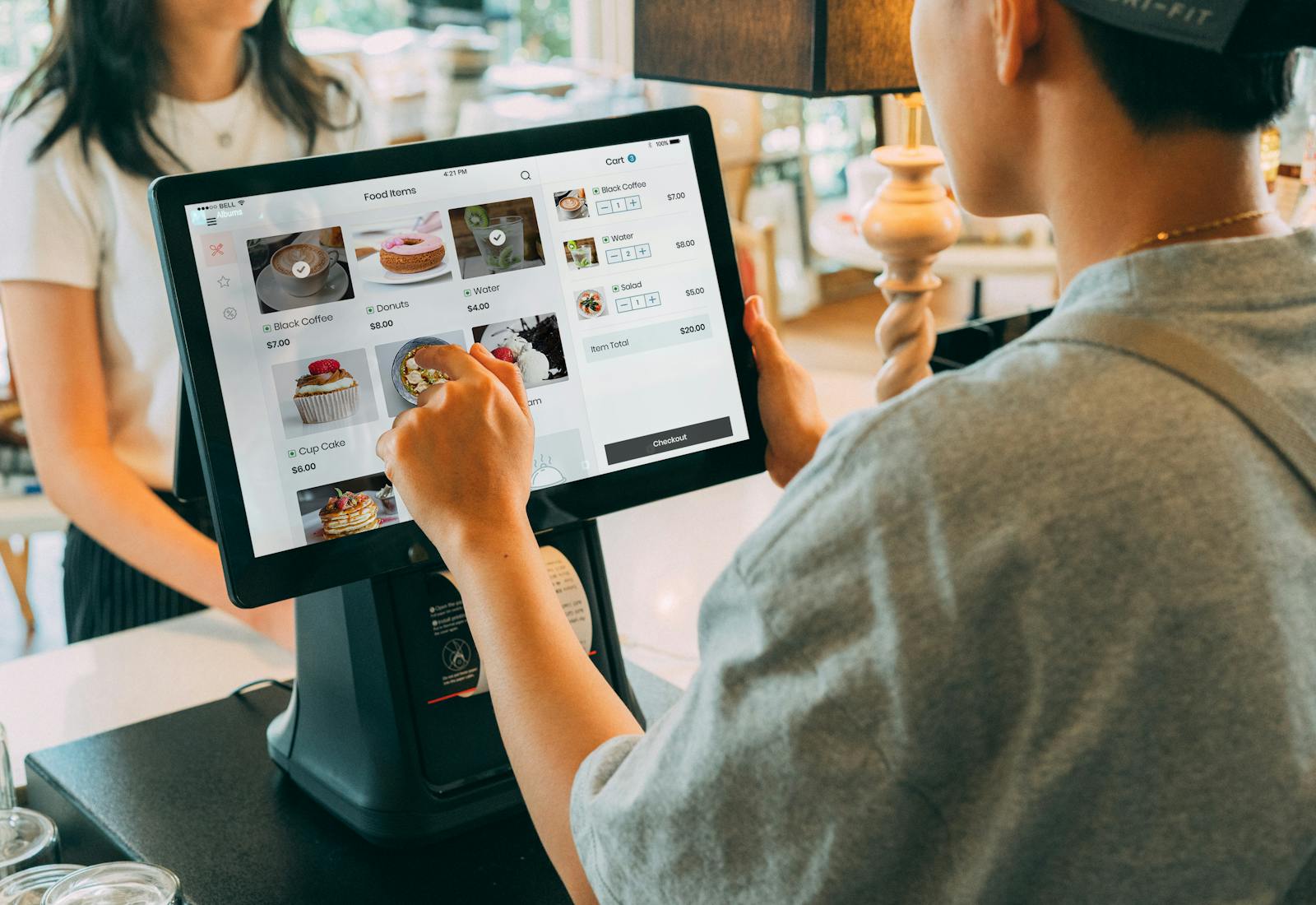 A shop assistant ringing up a customer on a touchscreen point-of-sale terminal at the counter.